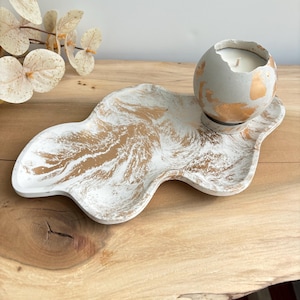 Może przedstawiać: Biała i złota marmurowa taca betonowa z okrągłym betonowym świecznikiem z złotymi akcentami. Świecznik zawiera białą świecę.