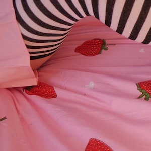Peut inclure: Une paire de bas rayés noirs et blancs jusqu'aux cuisses sur un couvre-lit rose à motif de fraises.