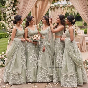 May include: Five matching sage green lehengas featuring sleeveless crop tops and floor-length skirts with intricate white floral embroidery. Each outfit includes a sheer matching dupatta draped over the arm. The text "Dreamexporters" is visible.