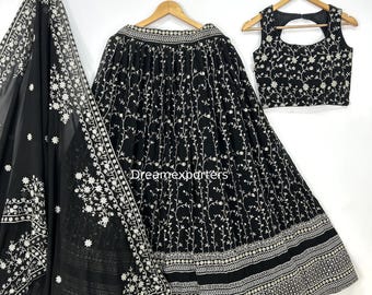 May include: A black three-piece outfit featuring a skirt, top, and shawl, all adorned with intricate white floral embroidery. The skirt and top are hanging on wooden hangers. The shawl is draped to the left. The text "Dreamexporters" is visible.