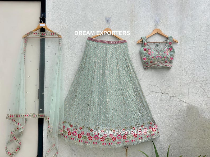 Op de afbeelding: Een lichtgroene geborduurde rok met een bijpassend geborduurd topje. De rok heeft een bloemenpatroon met roze en rode bloemen. Het topje is mouwloos en heeft een ronde hals. De tekst "DREAM EXPORTERS" is zichtbaar op de rok en het topje.