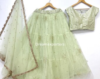 May include: A light green lehenga set with a matching dupatta. The skirt is tiered and decorated with gold sequins. The short-sleeved blouse is also gold and has a square pattern. The dupatta has a gold border.