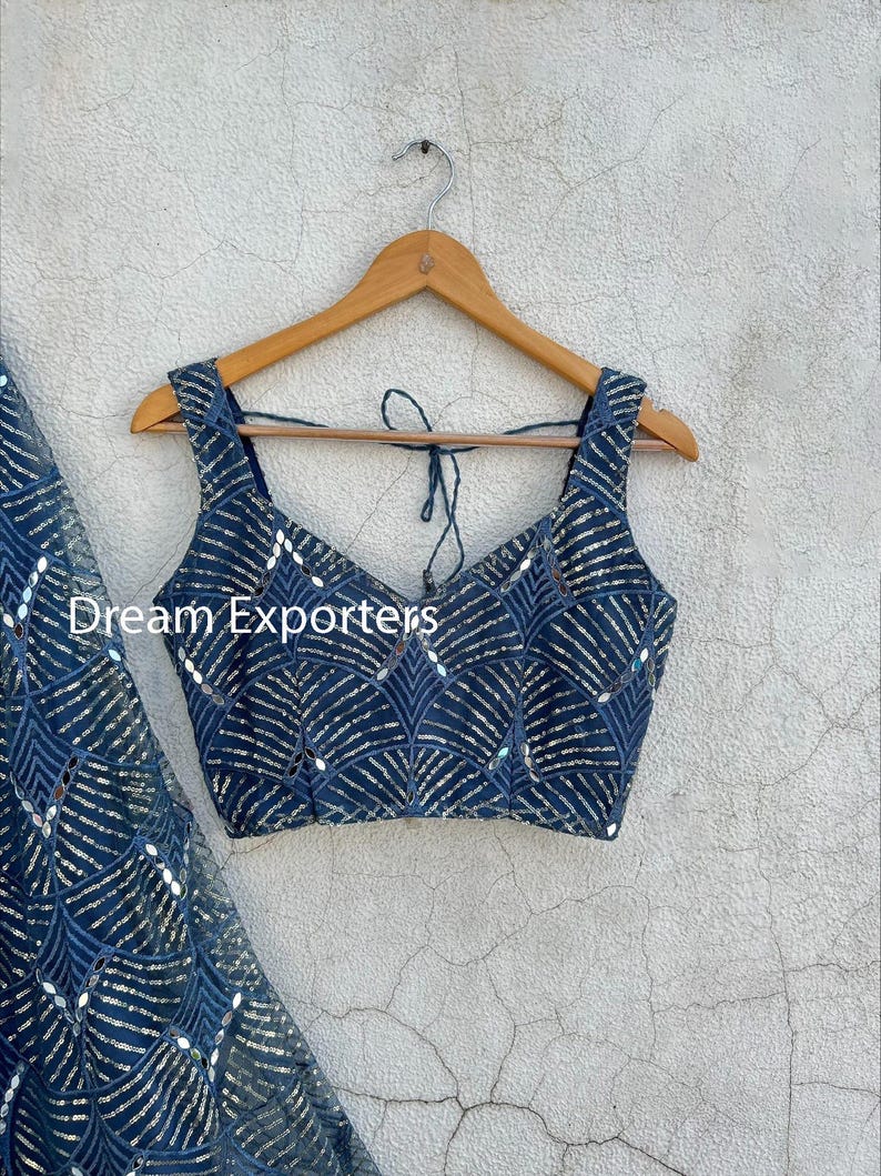 Puede incluir: Un top azul marino con cuello en V y tirantes anchos, adornado con lentejuelas plateadas en forma de abanico. El texto "Dream Exporters" es visible. El top est&aacute; colgado de una percha de madera.