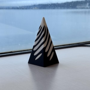Puede incluir: Un objeto negro con forma de pirámide con rayas blancas en los lados. El objeto está sobre una superficie blanca.