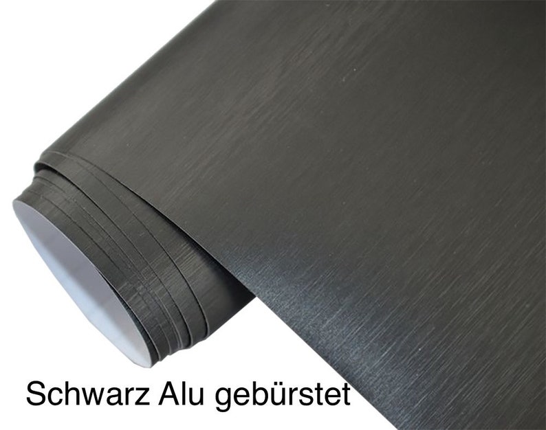 Puede incluir: Un rollo de vinilo negro cepillado de aluminio. El vinilo tiene un acabado texturizado que se asemeja al metal cepillado.