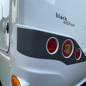 Puede incluir: Una autocaravana blanca con una franja negra y el texto "black edition" en el lateral. La autocaravana tiene tres luces traseras rojas.