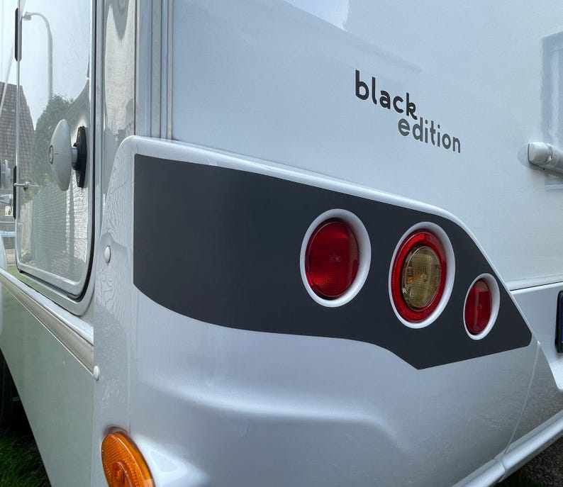 Puede incluir: Una autocaravana blanca con una franja negra y el texto "black edition" en el lateral. La autocaravana tiene tres luces traseras rojas.