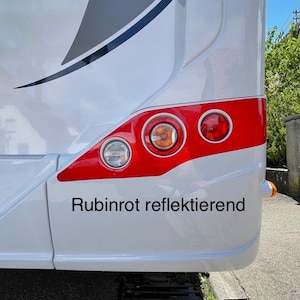 Puede incluir: Una autocaravana blanca con una franja roja y tres luces traseras rojas. El texto "Rubinrot reflektierend" est&aacute; impreso en la parte trasera de la autocaravana.