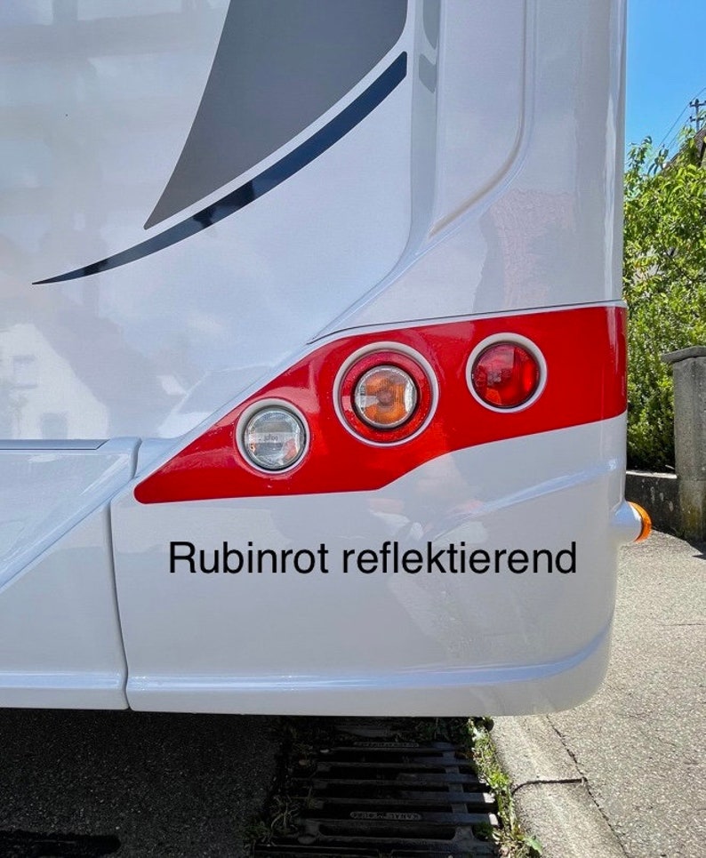 Puede incluir: Una autocaravana blanca con una franja roja y tres luces traseras rojas. El texto "Rubinrot reflektierend" est&aacute; impreso en la parte trasera de la autocaravana.