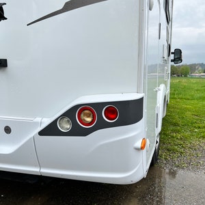 Puede incluir: Una autocaravana blanca con un borde negro alrededor de las luces traseras. Las luces traseras son rojas, &aacute;mbar y transparentes. La autocaravana est&aacute; aparcada en un camino de grava.