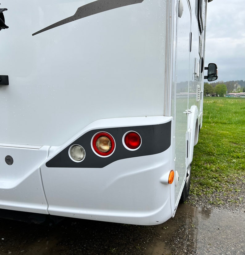 Puede incluir: Una autocaravana blanca con un borde negro alrededor de las luces traseras. Las luces traseras son rojas, &aacute;mbar y transparentes. La autocaravana est&aacute; aparcada en un camino de grava.