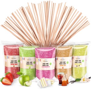 Peut inclure: Cinq sachets de sucre coloré pour barbe à papa, chacun avec une saveur différente, dont fraise, pomme, guimauve, cola et vanille. Des bâtonnets en bois sont disposés au-dessus des sachets. Fraises, tranches de pomme, guimauves, bouteilles de cola et gousses de vanille sont visibles.