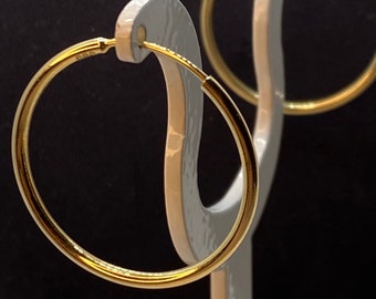 Pode incluir: Um par de brincos de argola de ouro em um expositor branco. Os brincos são simples e clássicos.