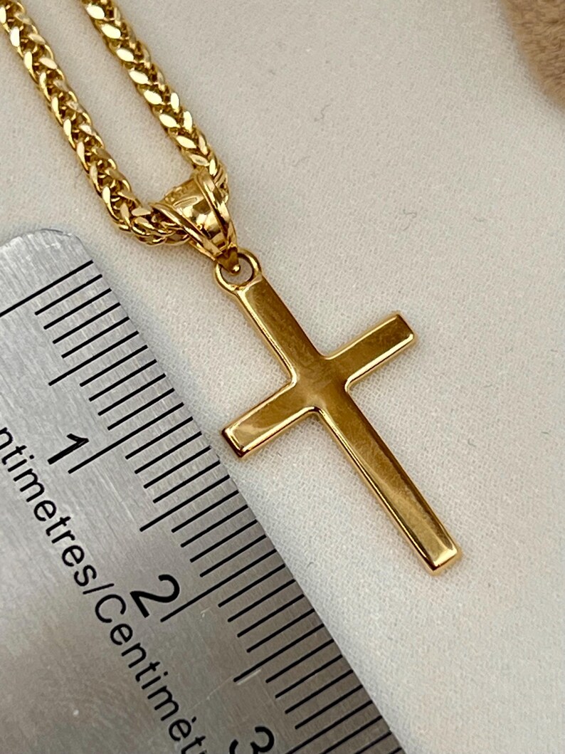 May include: A gold cross pendant on a matching chain. The cross has a simple, classic design with a polished finish. The chain is a wheat-link style. A ruler is in the image, showing centimetres.