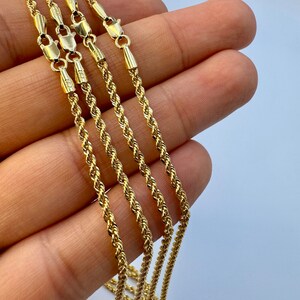 May include: Four gold rope chains of varying lengths, displayed on a hand. The chains are made of a twisted rope design.