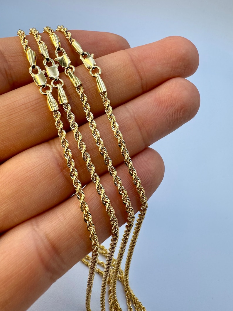 May include: Four gold rope chains of varying lengths, displayed on a hand. The chains are made of a twisted rope design.
