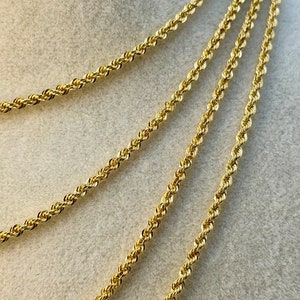 May include: Four gold rope chains of varying lengths, displayed on a beige fabric background.