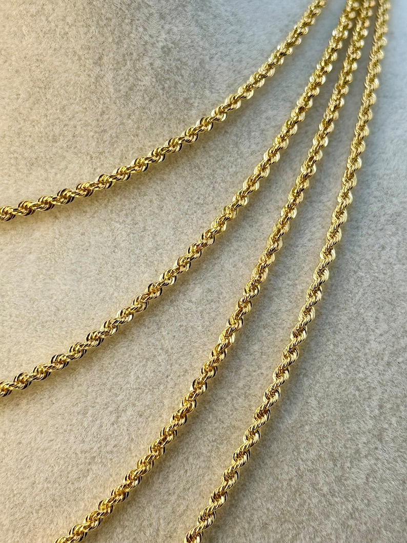 May include: Four gold rope chains of varying lengths, displayed on a beige fabric background.