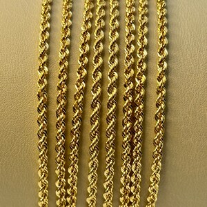 May include: A close-up of seven gold rope chains of varying lengths. The chains are arranged in a vertical stack, with the longest chain at the top and the shortest chain at the bottom.