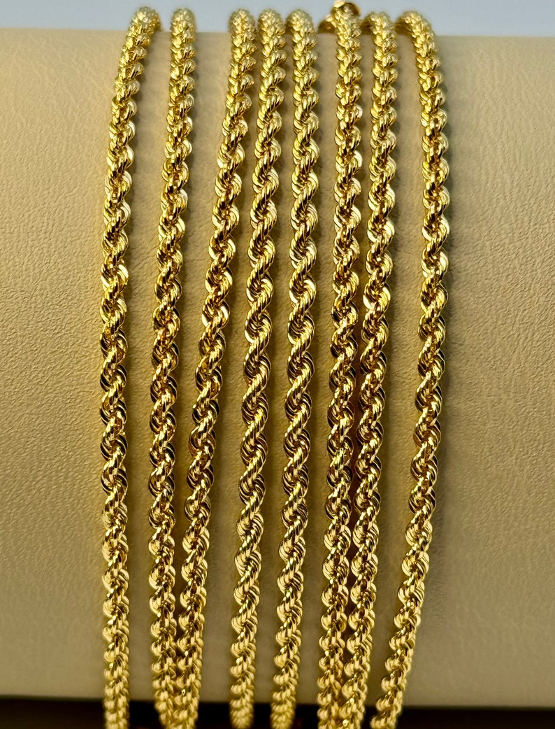 May include: A close-up of seven gold rope chains of varying lengths. The chains are arranged in a vertical stack, with the longest chain at the top and the shortest chain at the bottom.