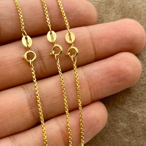 May include: Three gold-colored box chains, each featuring a round spring ring clasp and a small rectangular tag stamped with the text 925. The chains have a uniform square link design and a polished metallic finish, presented as a set of jewelry.