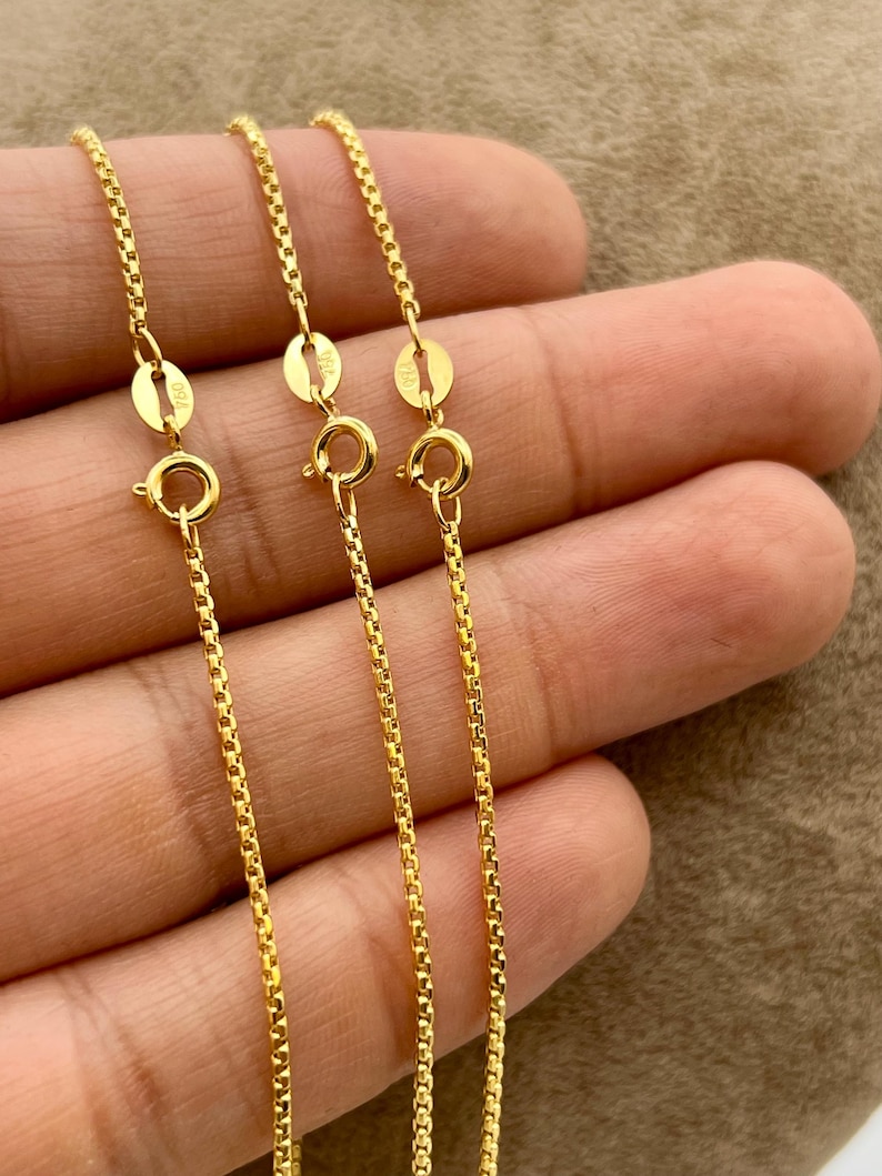 May include: Three gold-colored box chains, each featuring a round spring ring clasp and a small rectangular tag stamped with the text 925. The chains have a uniform square link design and a polished metallic finish, presented as a set of jewelry.