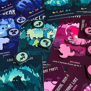 Könnte beinhalten: Eine Sammlung farbenfroher Brettspielkarten und -marker. Die Karten zeigen Illustrationen von Zeichentieren und Text. Die Marker sind rund mit verschiedenen Symbolen. Die Farbpalette umfasst Blau-, Rosa- und Grüntöne. Der Text enthält die Wörter "Sleepy-Time Security" und "Totally Silly".
