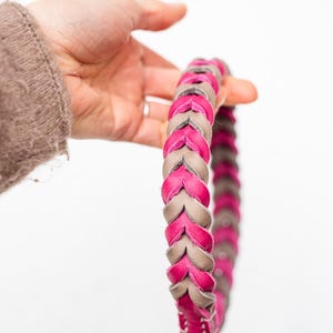 May include: A pink and gray braided leather dog collar with a gold metal clasp.