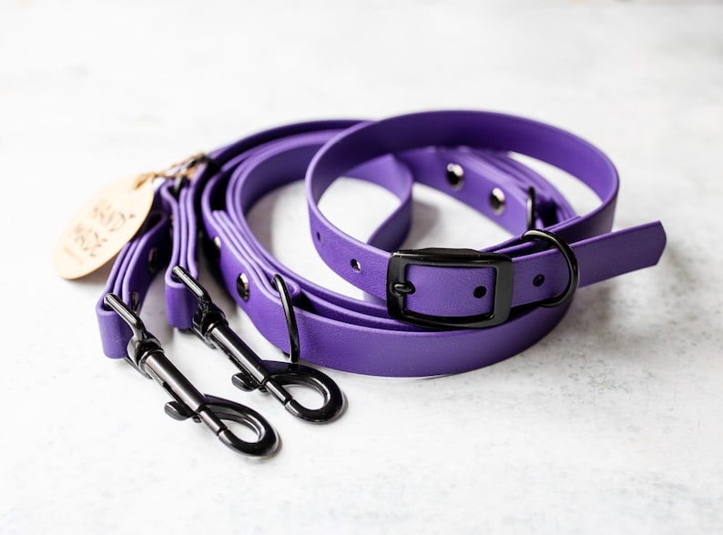 May include: Purple dog leashes and collars with black metal hardware. The leashes have a matching collar with a black buckle. A wooden tag with the words "Hand Made" is attached to the leash.