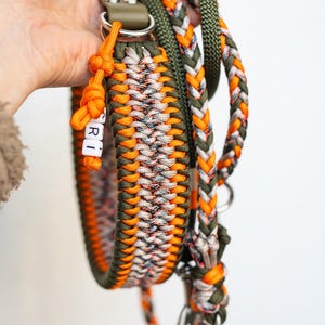 May include: A handmade dog collar and leash set. The collar and leash are made of braided nylon in shades of orange, green, white, and gray. The collar has the name "RI" spelled out in white letter beads. The leash has a silver-colored metal clasp.