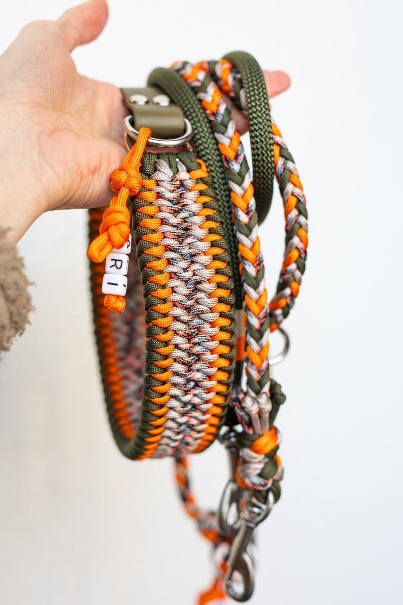 May include: A handmade dog collar and leash set. The collar and leash are made of braided nylon in shades of orange, green, white, and gray. The collar has the name "RI" spelled out in white letter beads. The leash has a silver-colored metal clasp.