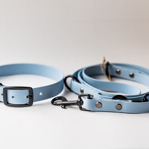 May include: A light blue dog collar and matching leash set. The collar has a black buckle, and the leash has a black clasp. The set is made of a smooth material and is designed for pet owners.