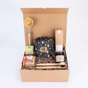 May include: A brown cardboard box filled with eco-friendly bathroom and cleaning supplies. The box contains a roll of toilet paper with the words "who gives a crap" printed on it, a bar of soap, a bottle of hand soap, a wooden brush, a jar of hand cream, and two toothbrushes.