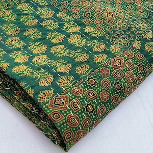 Könnte beinhalten: Gefalteter Textil mit grünem und goldenem Muster. Der Stoff weist ein sich wiederholendes Blumen- und geometrisches Design in Grün-, Gold- und Brauntönen auf. Weiße Nähte umreißen die Muster. Der Stoff ist gefaltet und zeigt mehrere Schichten.