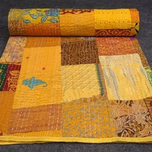 Könnte beinhalten: Ein Patchwork-Quilt in Gelb-, Orange- und Brauntönen mit einem aufgerollten Abschnitt oben. Der Quilt weist verschiedene Stoffmuster auf, darunter Blumen- und geometrische Designs, und ist wahrscheinlich handgefertigt.
