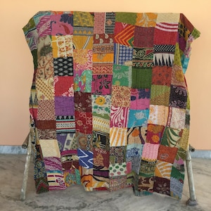 Könnte beinhalten: Ein Patchwork-Quilt mit einer lebendigen Mischung aus Farben und Mustern. Der Quilt besteht aus verschiedenen Stoffquadraten, jedes mit einzigartigen Designs und Farbtönen, darunter Rot, Grün, Gelb und Lila. Der Quilt ist über einem Holzrahmen drapiert.