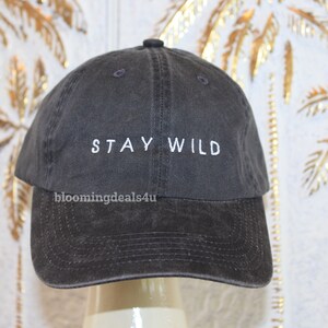 以下が含まれることがあります： 白い刺繍で「STAY WILD」と書かれた濃いグレーの野球帽です。