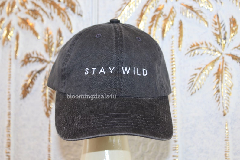 以下が含まれることがあります： 白い刺繍で「STAY WILD」と書かれた濃いグレーの野球帽です。