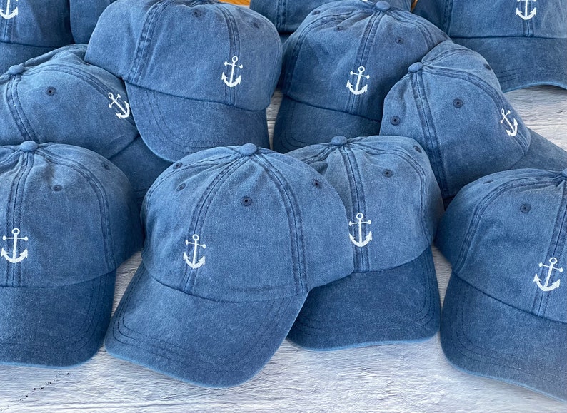 May include: A group of blue denim baseball caps with white embroidered anchors. The caps have a classic style and are perfect for casual wear.