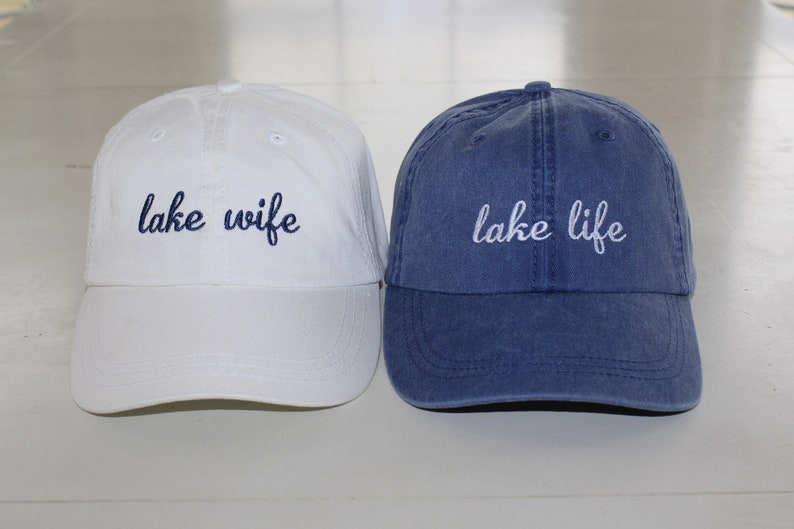 K&ouml;nnte beinhalten: Zwei Baseballkappen, eine wei&szlig;e mit "lake wife" in blau gestickt, und eine blaue mit "lake life" in wei&szlig; gestickt.