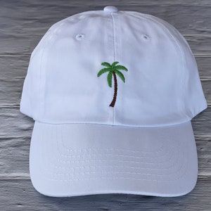 May include: White baseball cap with an embroidered green palm tree on the front.