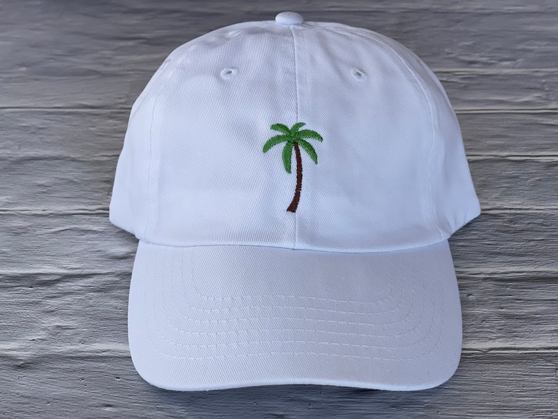 May include: White baseball cap with an embroidered green palm tree on the front.