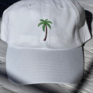 May include: White baseball cap with an embroidered green palm tree on the front.