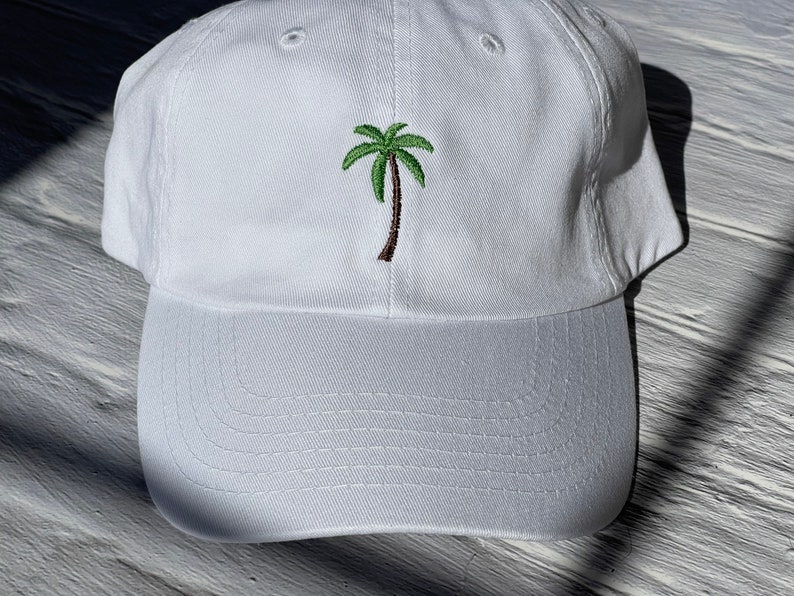 May include: White baseball cap with an embroidered green palm tree on the front.