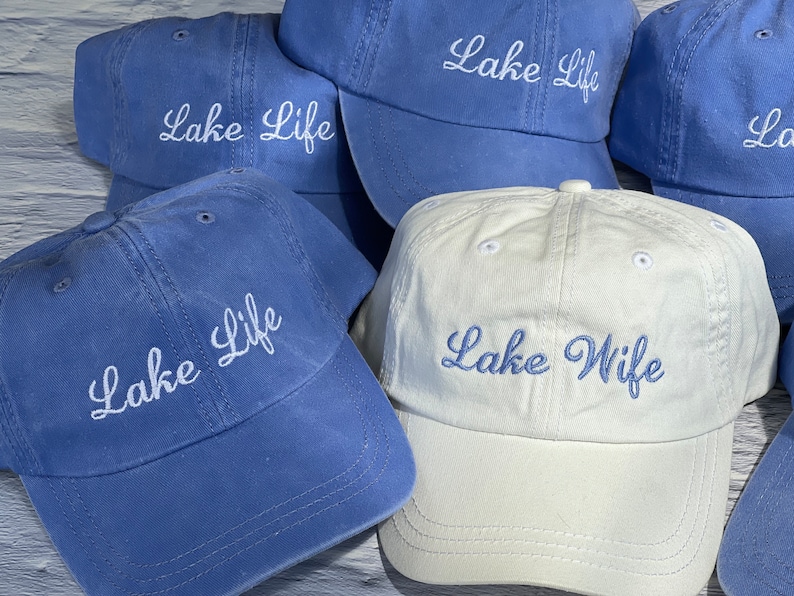 K&ouml;nnte beinhalten: F&uuml;nf blaue und wei&szlig;e Baseballkappen mit gesticktem Text. Die Kappen sagen "Lake Life" und "Lake Wife".