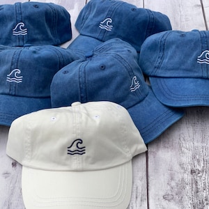 May include: Five blue denim baseball caps with a white wave design. One white baseball cap with a blue wave design.