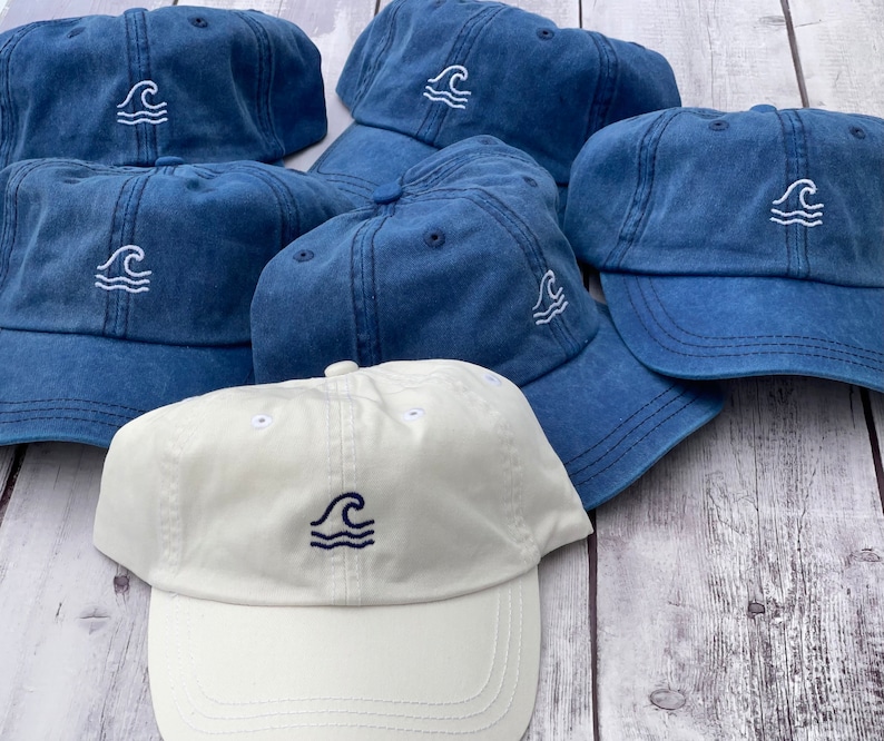 May include: Five blue denim baseball caps with a white wave design. One white baseball cap with a blue wave design.