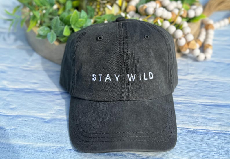 以下が含まれることがあります： 白い刺繍で「STAY WILD」と書かれた黒いコットン製のベースボールキャップです。