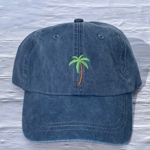 May include: A dark blue denim baseball cap with an embroidered green palm tree on the front.