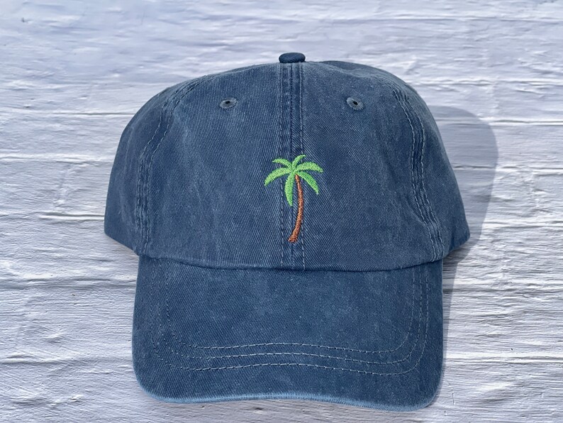 May include: A dark blue denim baseball cap with an embroidered green palm tree on the front.